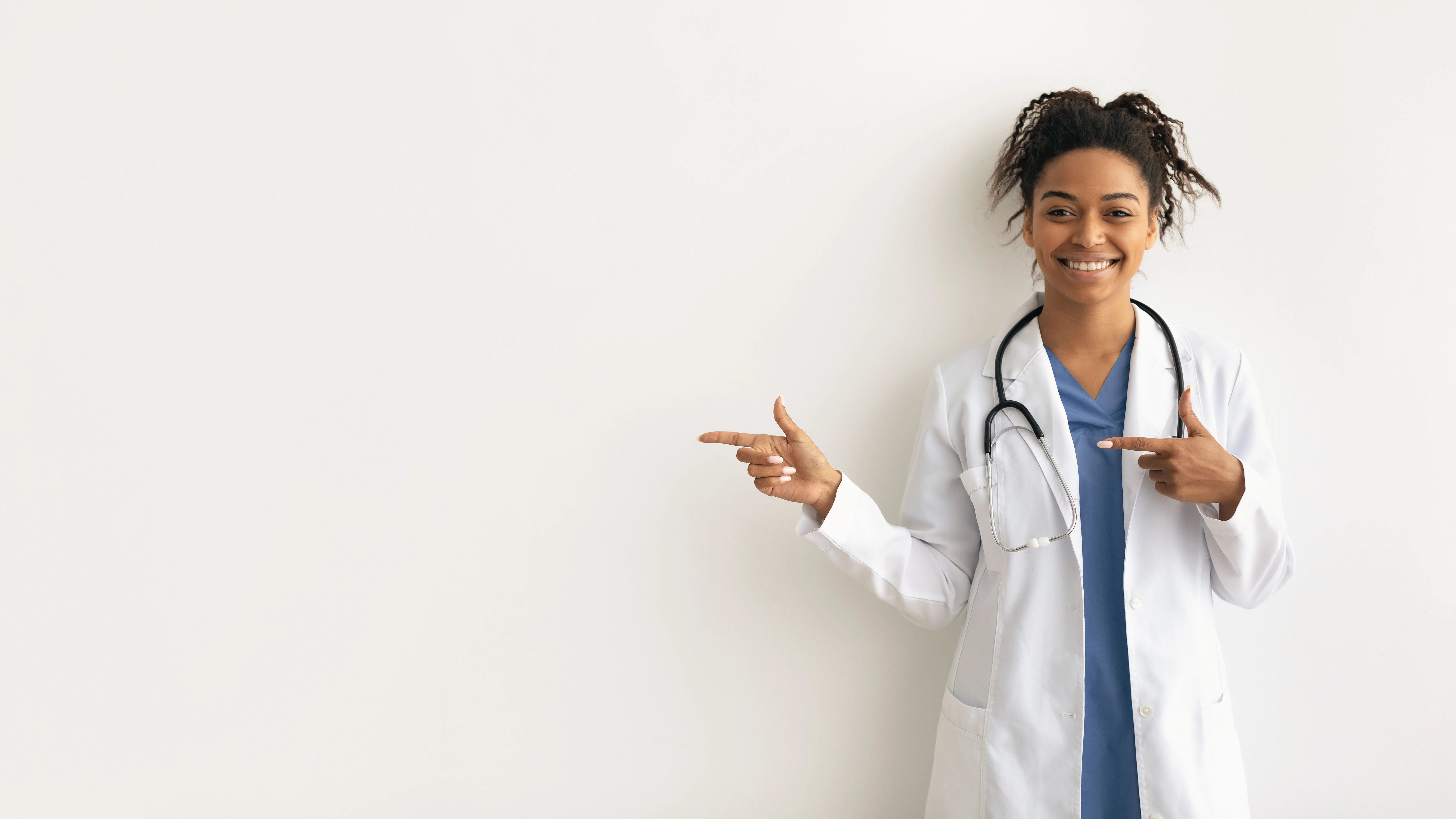 Profesional de la salud sonriente en bata blanca señala a un lado contra un fondo blanco liso