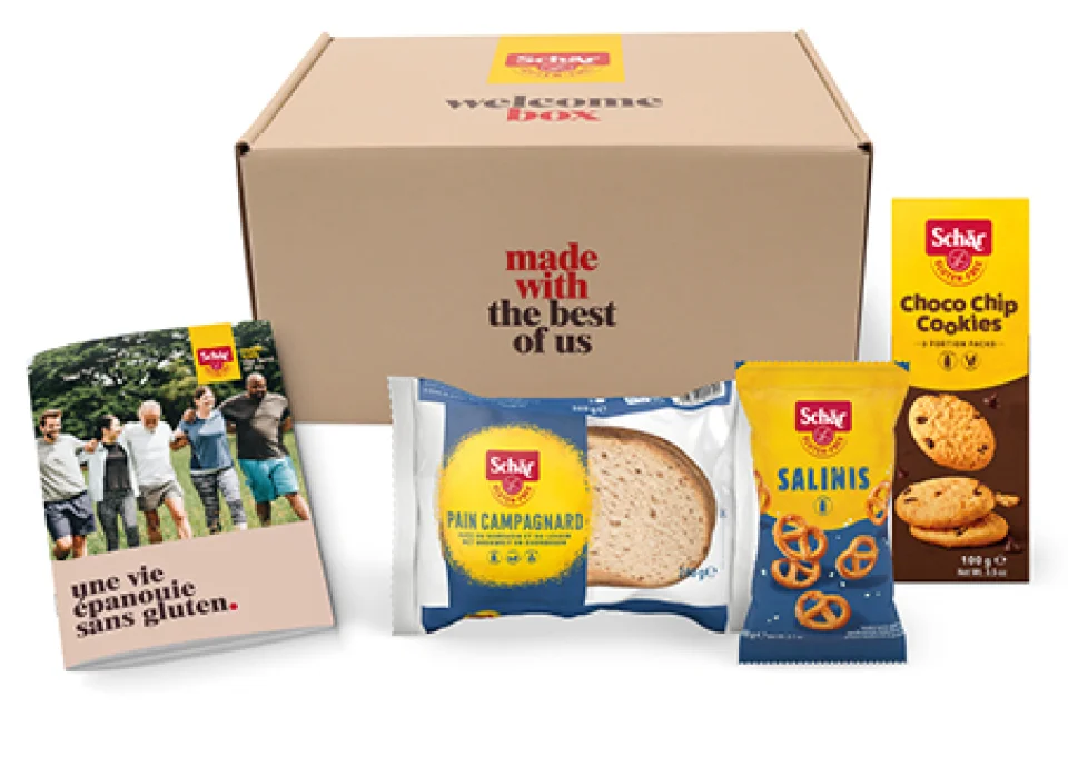Une boîte de bienvenue contenant du pain, des biscuits et des bretzels sans gluten, avec un livret informatif sur Schär