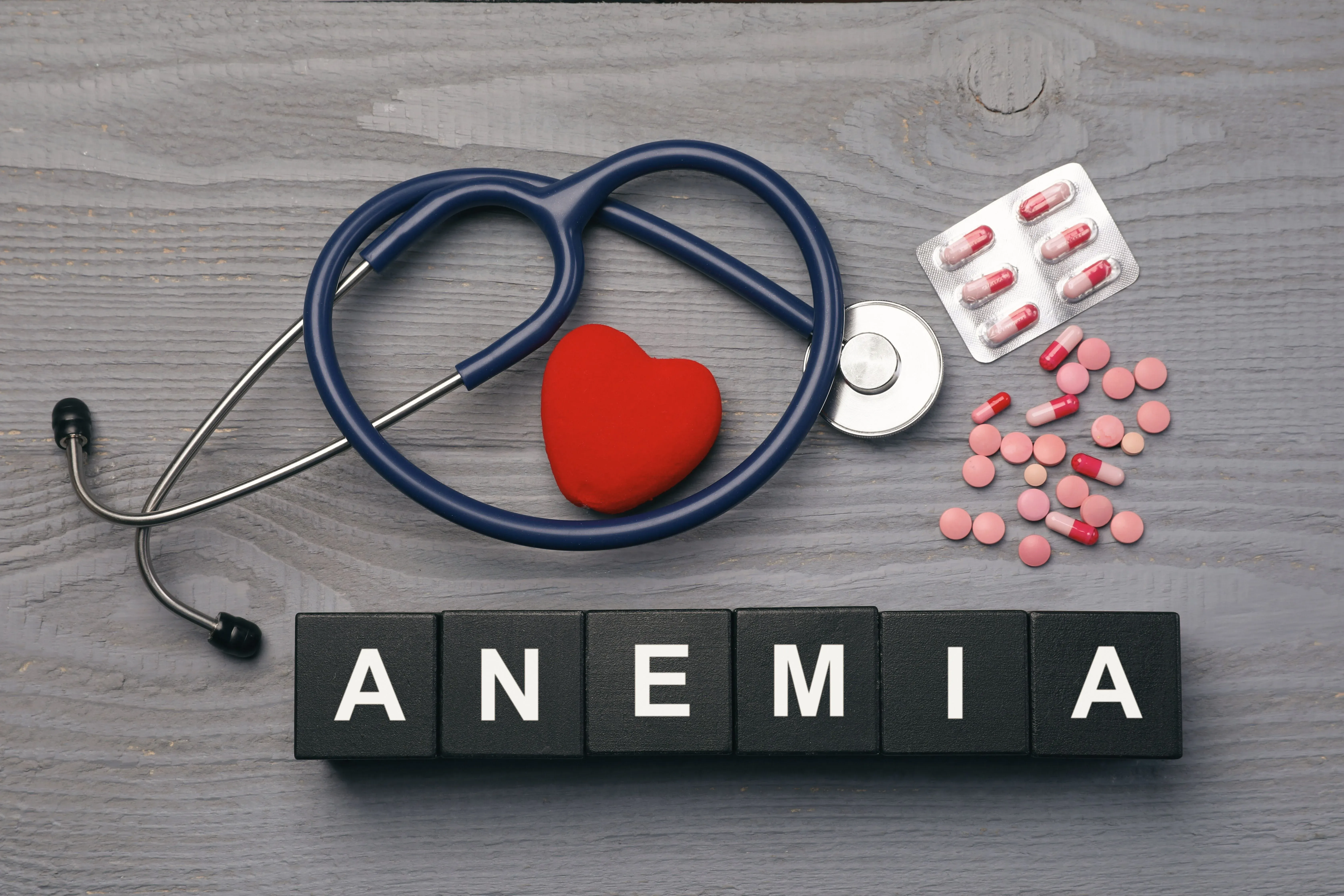Estetoscopio y corazón rojo junto a pastillas y bloques negros que dicen 'ANEMIA' sobre una superficie de madera