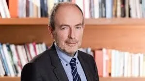 Uomo di mezza età in giacca che sta con sicurezza davanti a una libreria piena di libri sullo sfondo