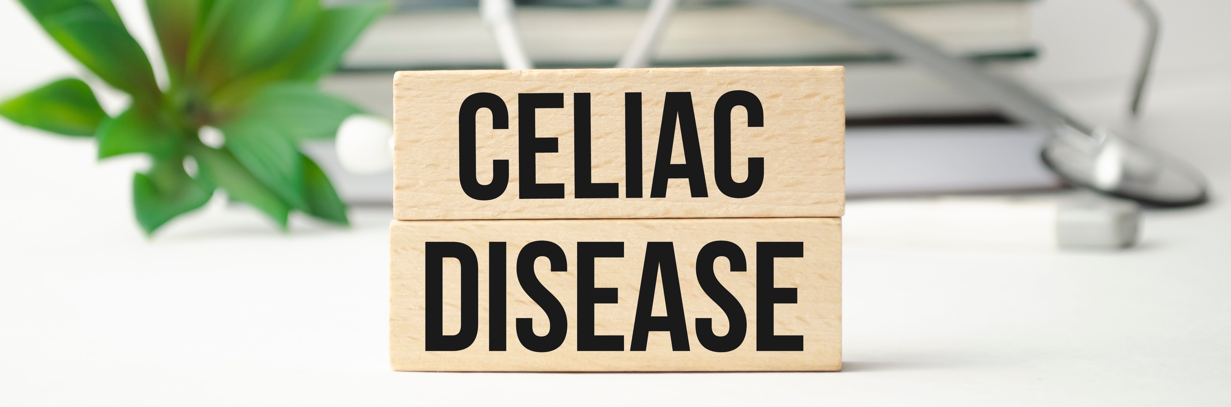 Block letters spell "CELIAC DISEASE" on wooden blocks, with a green plant and medical tools blurred in the background