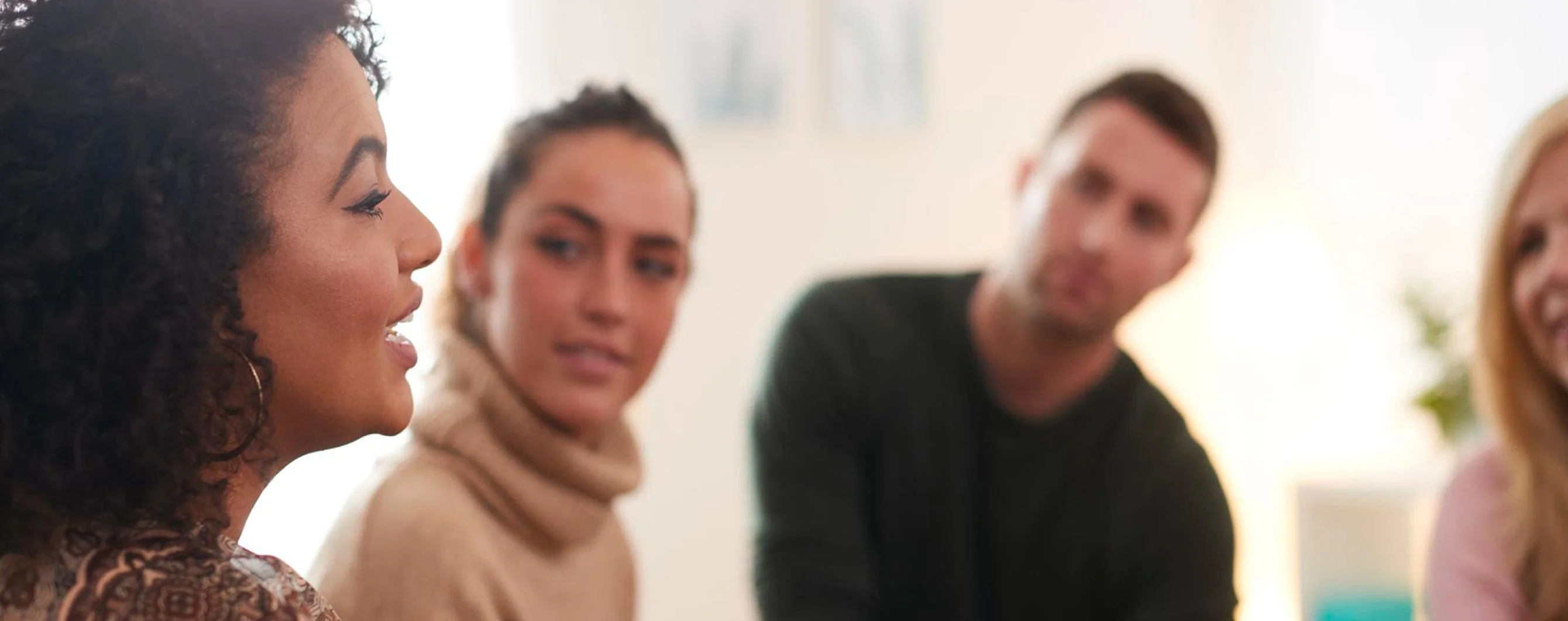 A diverse group of four people engaged in a conversation, with one woman speaking animatedly in a cozy setting