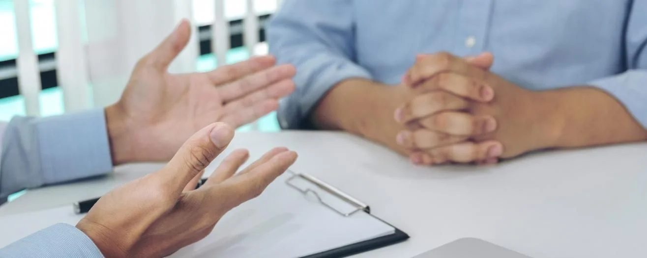 Deux personnes discutent, l'une gesticule avec les mains, l'autre écoute attentivement les mains jointes