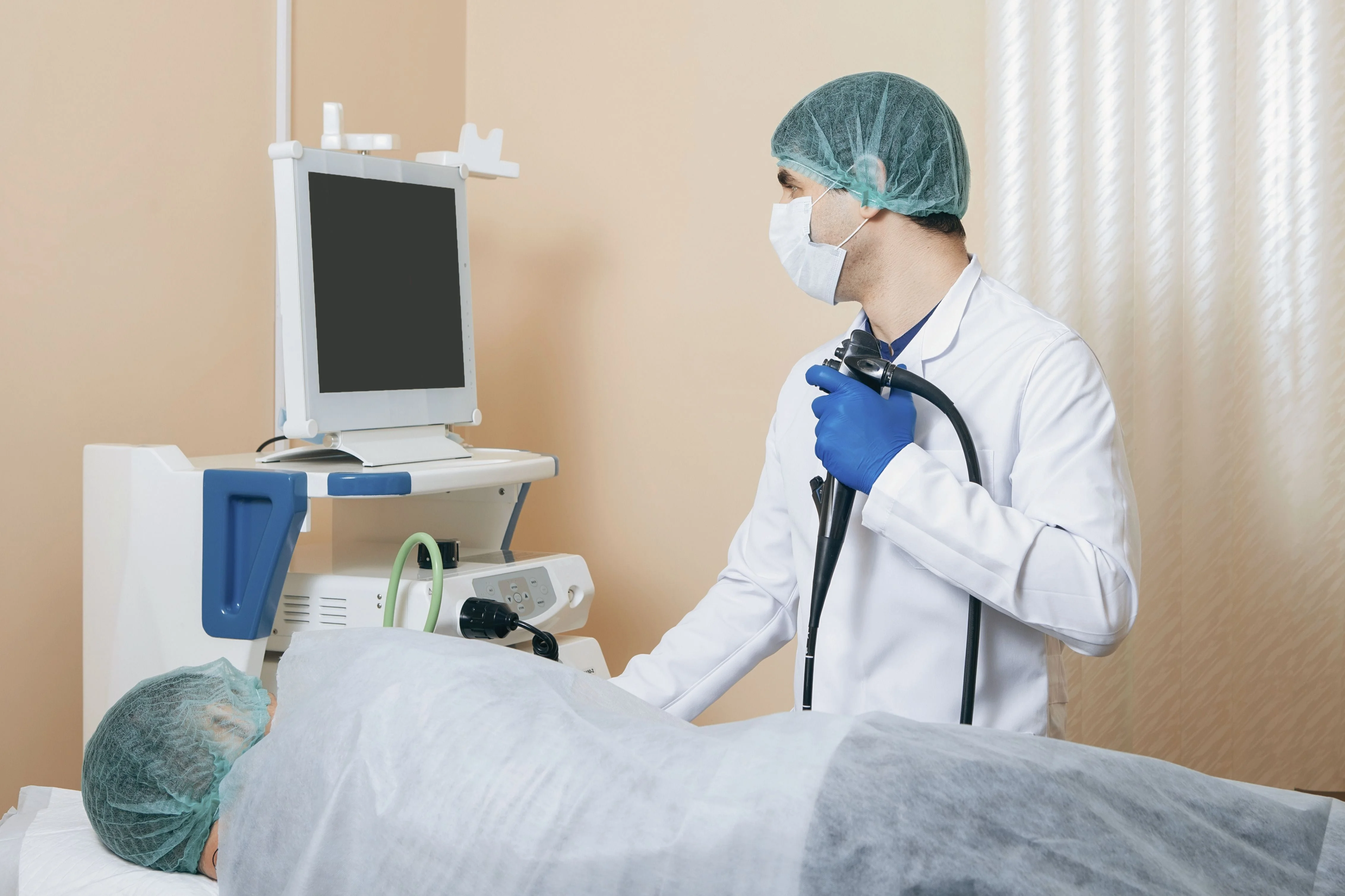 Un médico se prepara para un procedimiento con un endoscopio, monitoreando a un paciente cubierto con una manta