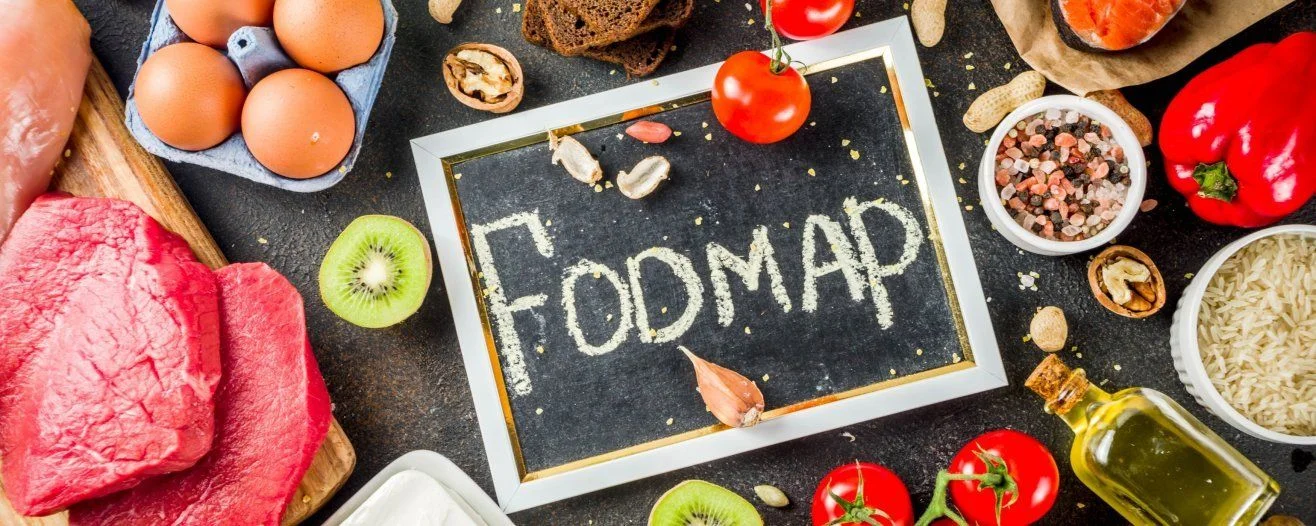 A blackboard with 'FODMAP' written in chalk surrounded by various fresh foods and ingredients