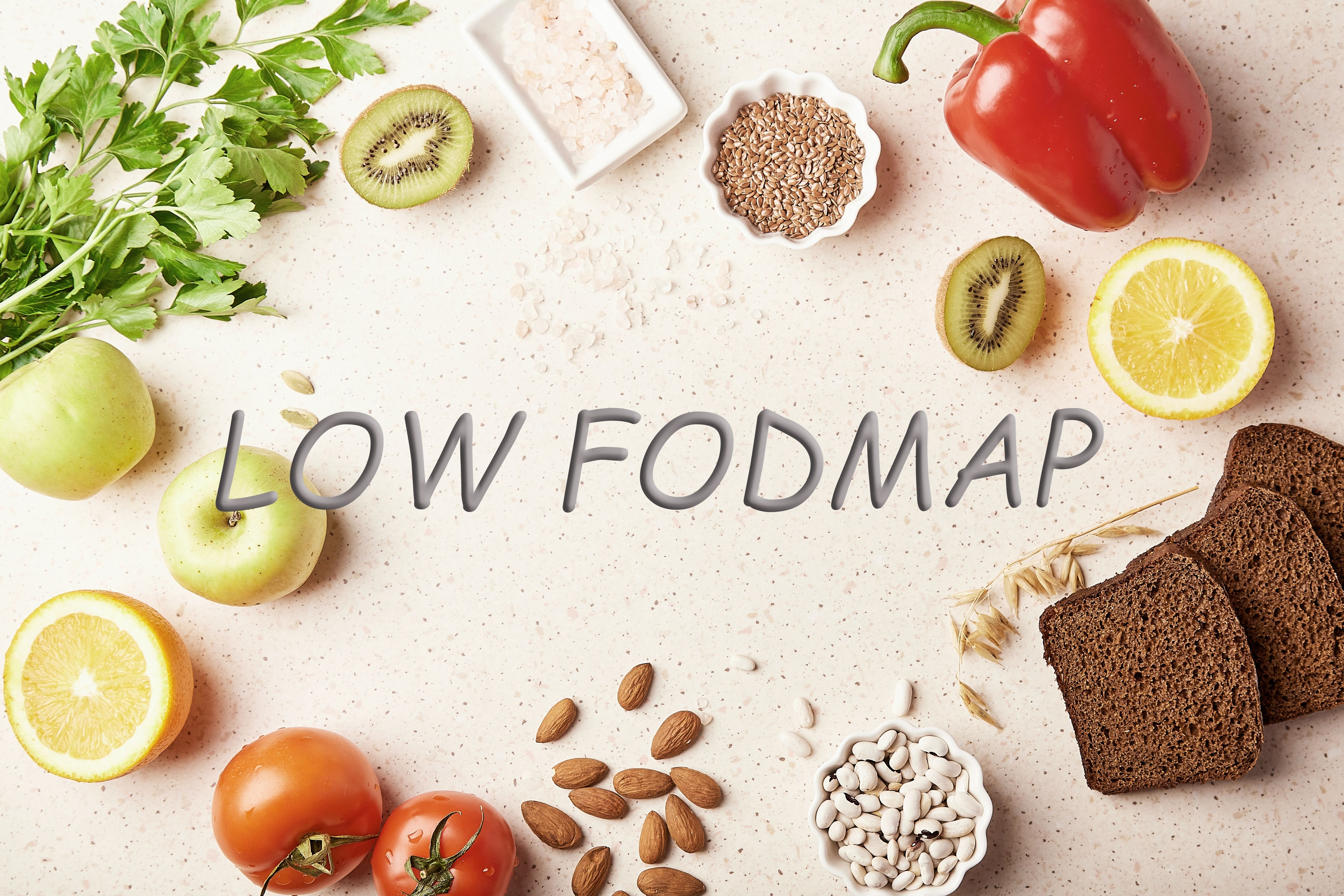 Fresh ingredients for a low FODMAP diet, featuring green apples, peppers, tomatoes, herbs, lemons, and grains on a light surface