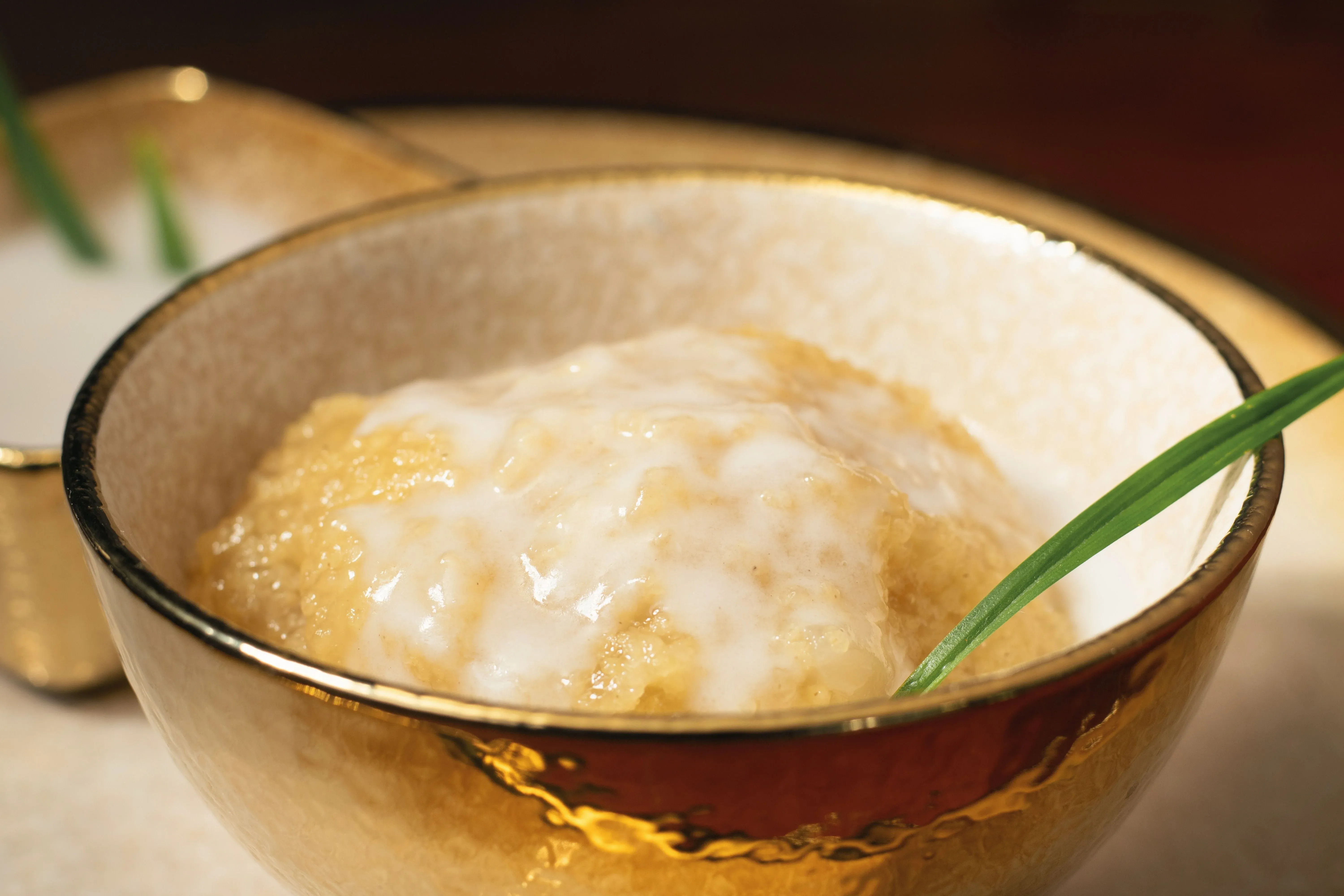 Primer plano de un postre cremoso en un bol dorado, cubierto con leche de coco y adorno verde