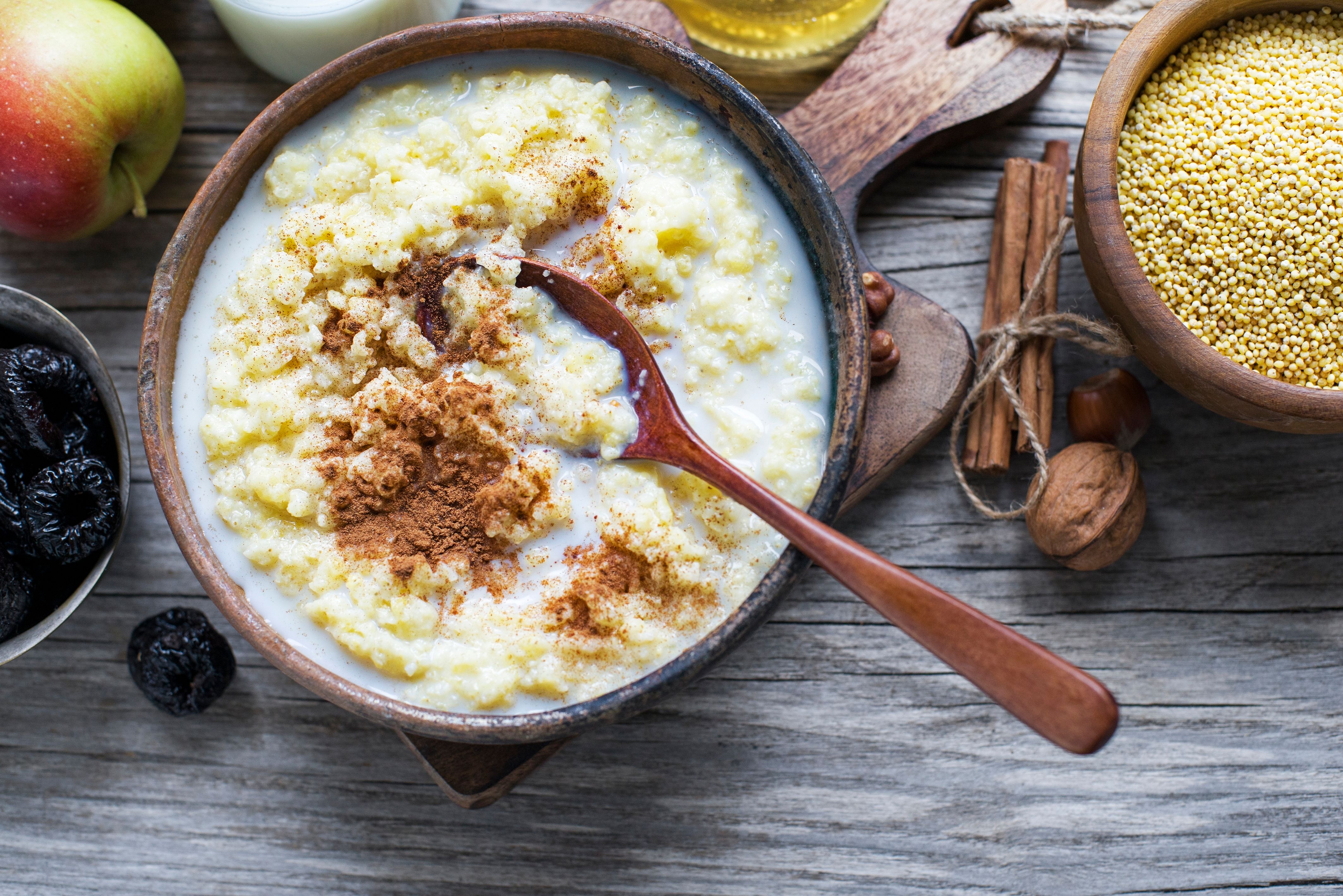 Creamy millet porridge topped with cinnamon, surrounded by an apple, dried fruits, millet grains, and cinnamon sticks