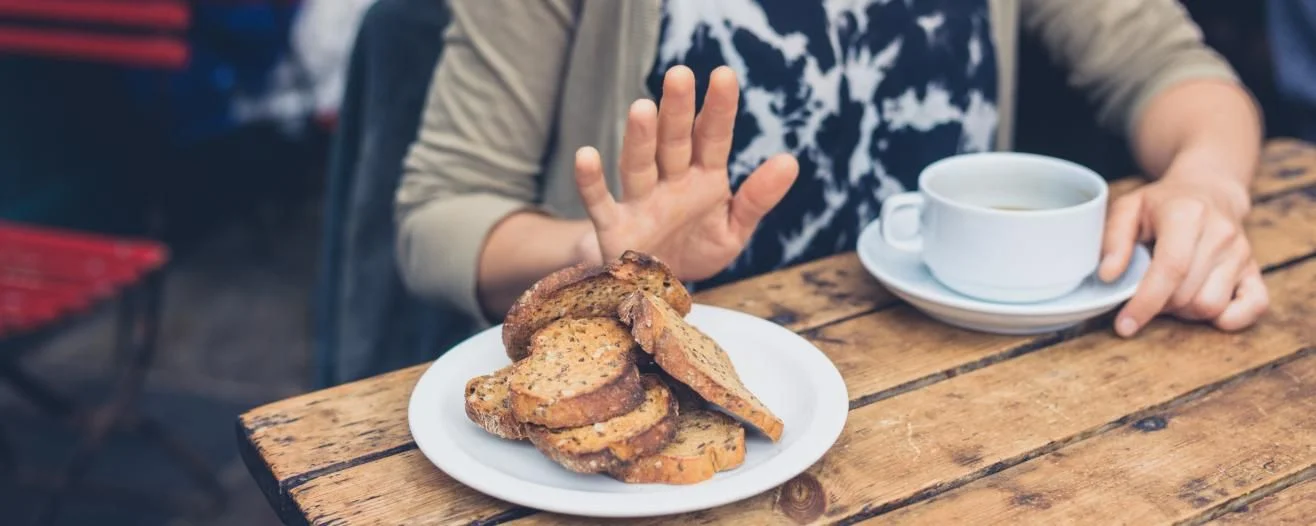 A hand gestures 'no' above a plate of cookies on a wooden table beside a cup of coffee