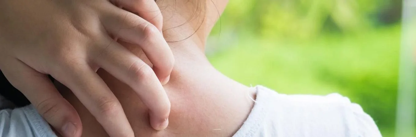 A hand scratching the neck of a person, with soft focus on a lush green background