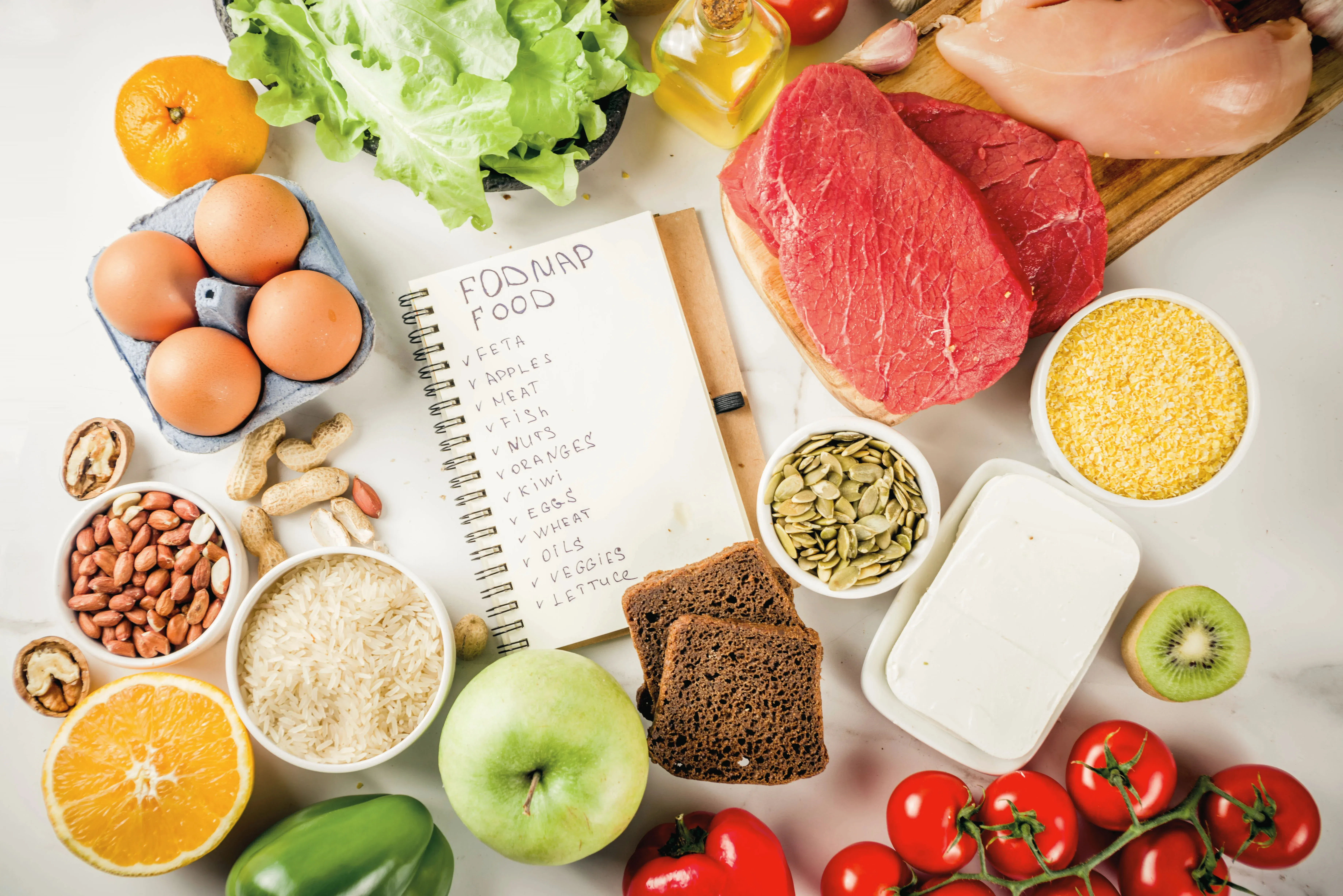An assortment of fresh foods including eggs, tomatoes, lettuce, and a notebook listing FODMAP foods