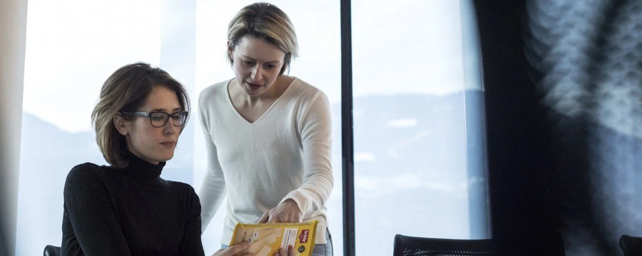 Due donne in un ufficio moderno discutono un documento, una indica il foglio mentre è seduta