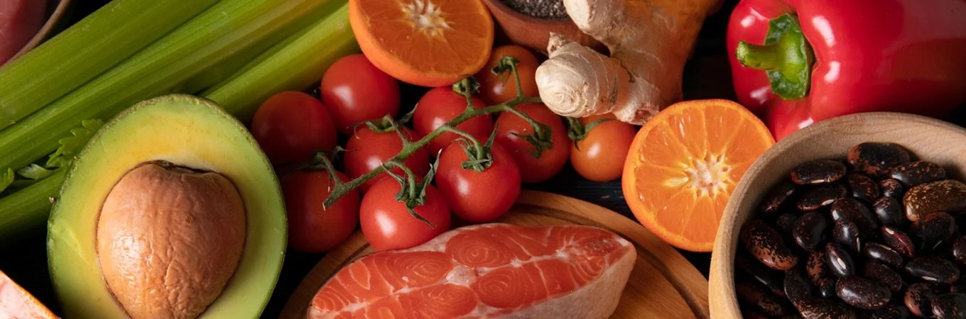 A colorful assortment of fresh vegetables and fruits including avocado, tomatoes, oranges, and fish