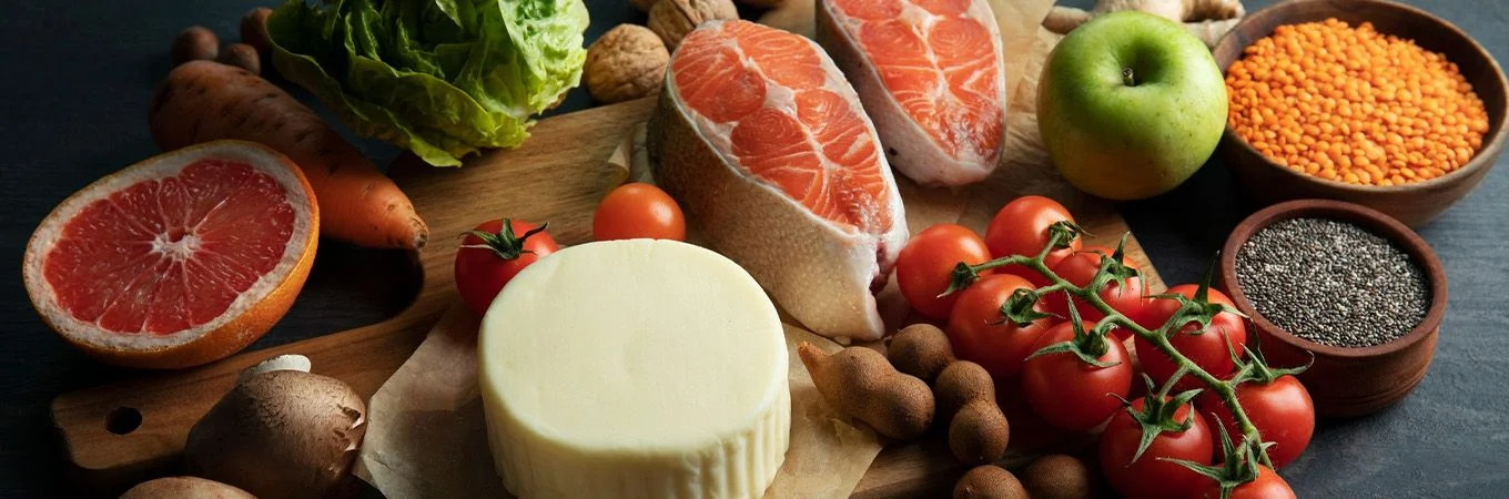 Ein Holzbrett mit buntem Gemüse und Obst, darunter Lachs, Käse, Tomaten und ein Apfel
