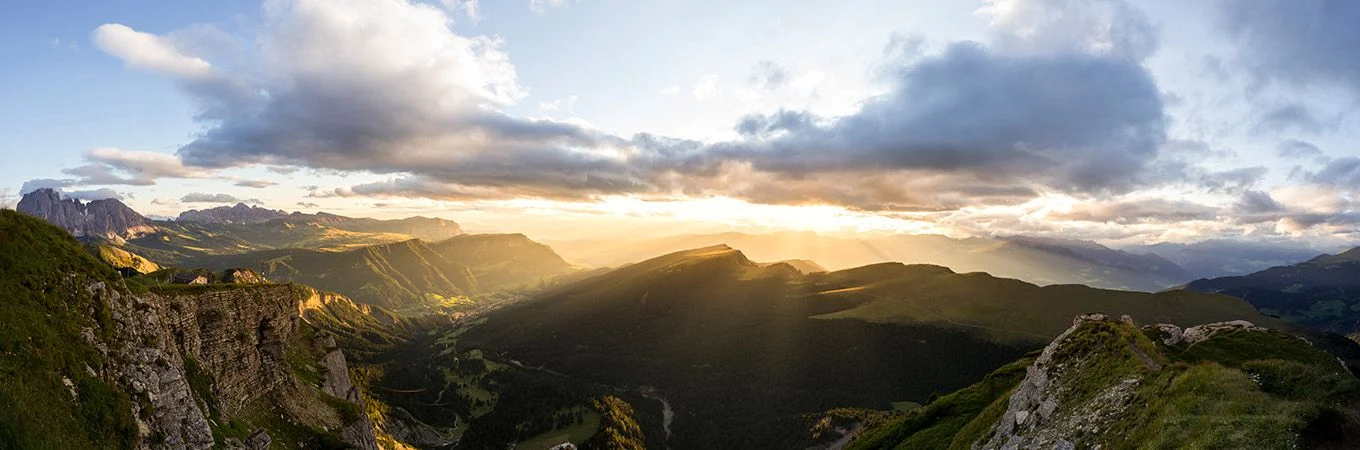 Impresionante paisaje montañoso con una vibrante puesta de sol, rayos de luz iluminan valles y picos rocosos