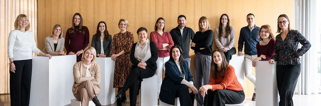 Un grupo diverso de 18 mujeres y hombres posando en un interior moderno con paredes de madera y luz brillante