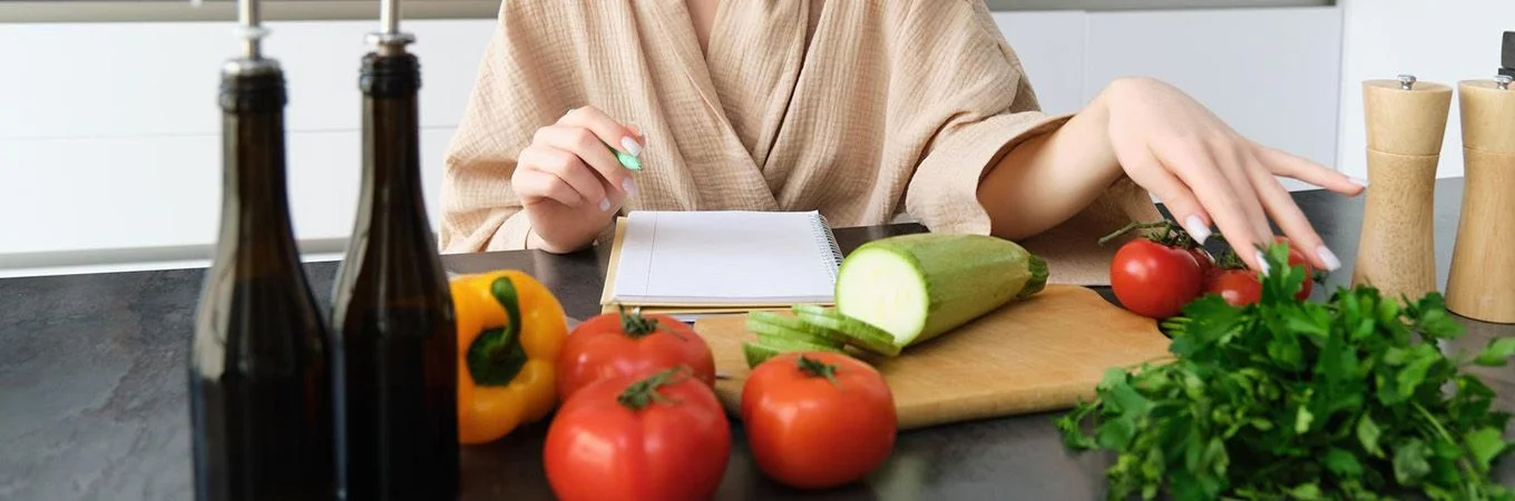 Eine Person im Bademantel bereitet Zutaten auf einem Küchentisch vor, mit frischen Tomaten, Paprika und Kräutern