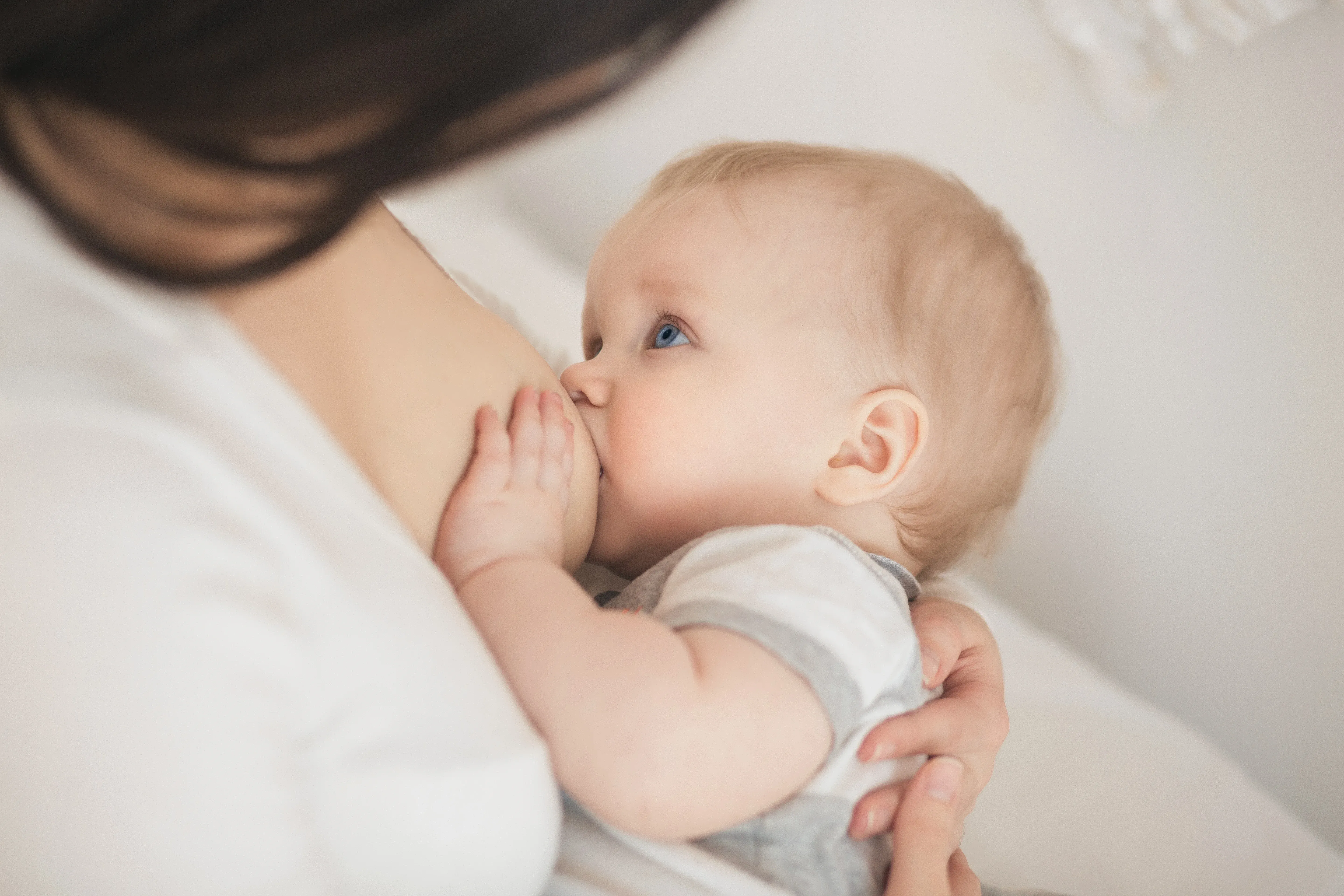 Un bambino con occhi azzurri allatta, tenuto da un genitore in un ambiente intimo e illuminato delicatamente
