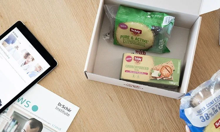 Eine Abo-Box mit Schär-Produkten, darunter knuspriges Brot und aktive Snacks, auf einem Holztisch