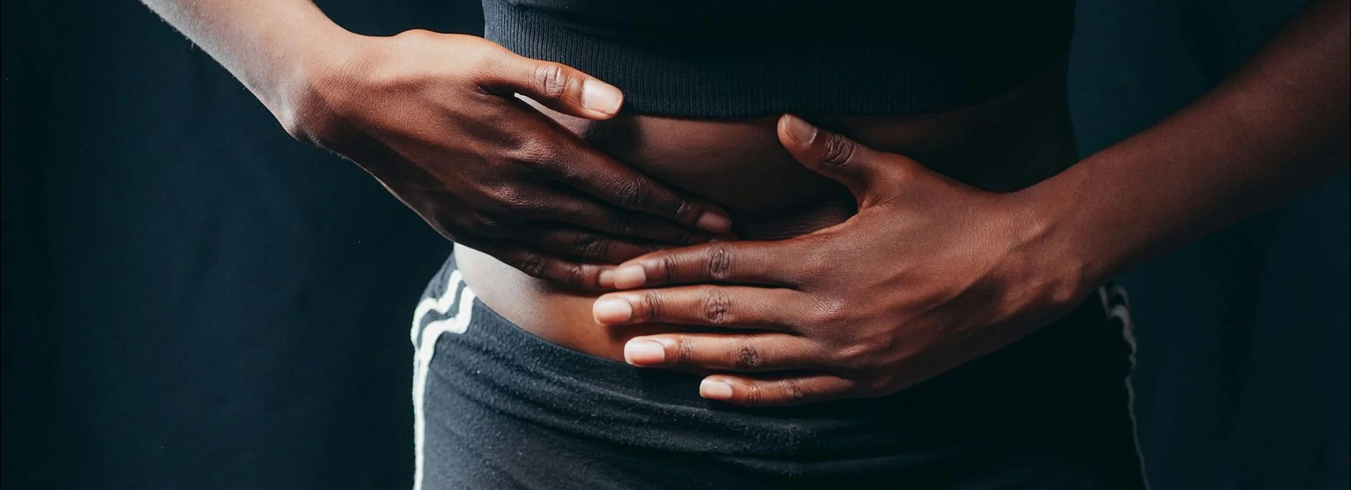 Hands resting on a bare stomach, expressing discomfort in a dark setting