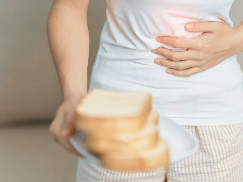 A person in a white shirt holds a plate of toast while clutching their stomach in discomfort