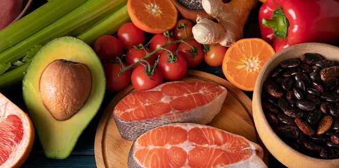 A variety of fresh ingredients including salmon, avocados, tomatoes, citrus fruits, and vegetables on a wooden surface