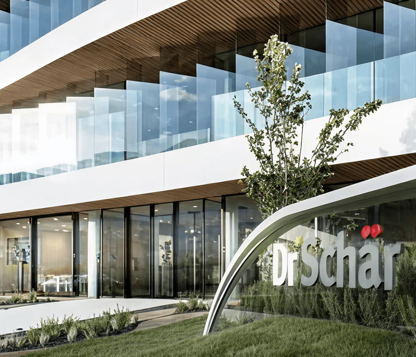 Modern building with large glass windows, a green front lawn, and the Dr.Schär sign prominently displayed
