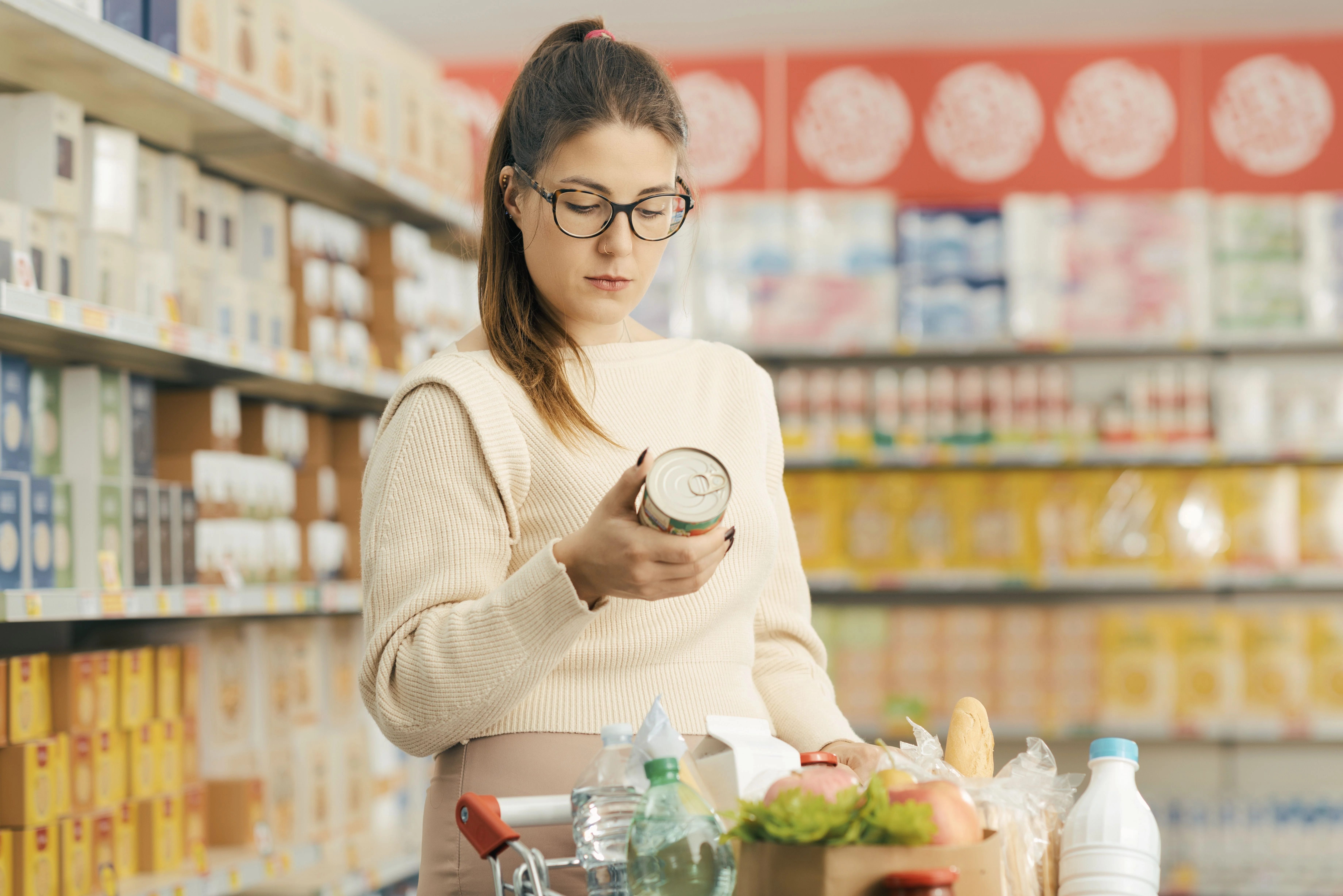 Una donna esamina una lattina in un corridoio del supermercato pieno di imballaggi colorati e alimenti